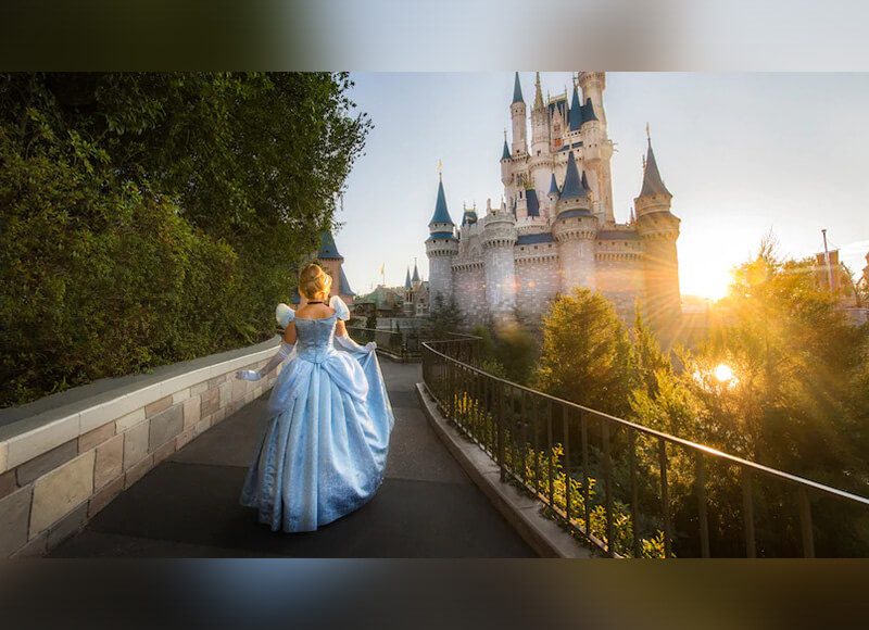 A wide shot of a woman wearing a Cinderella costume with a castle in the background